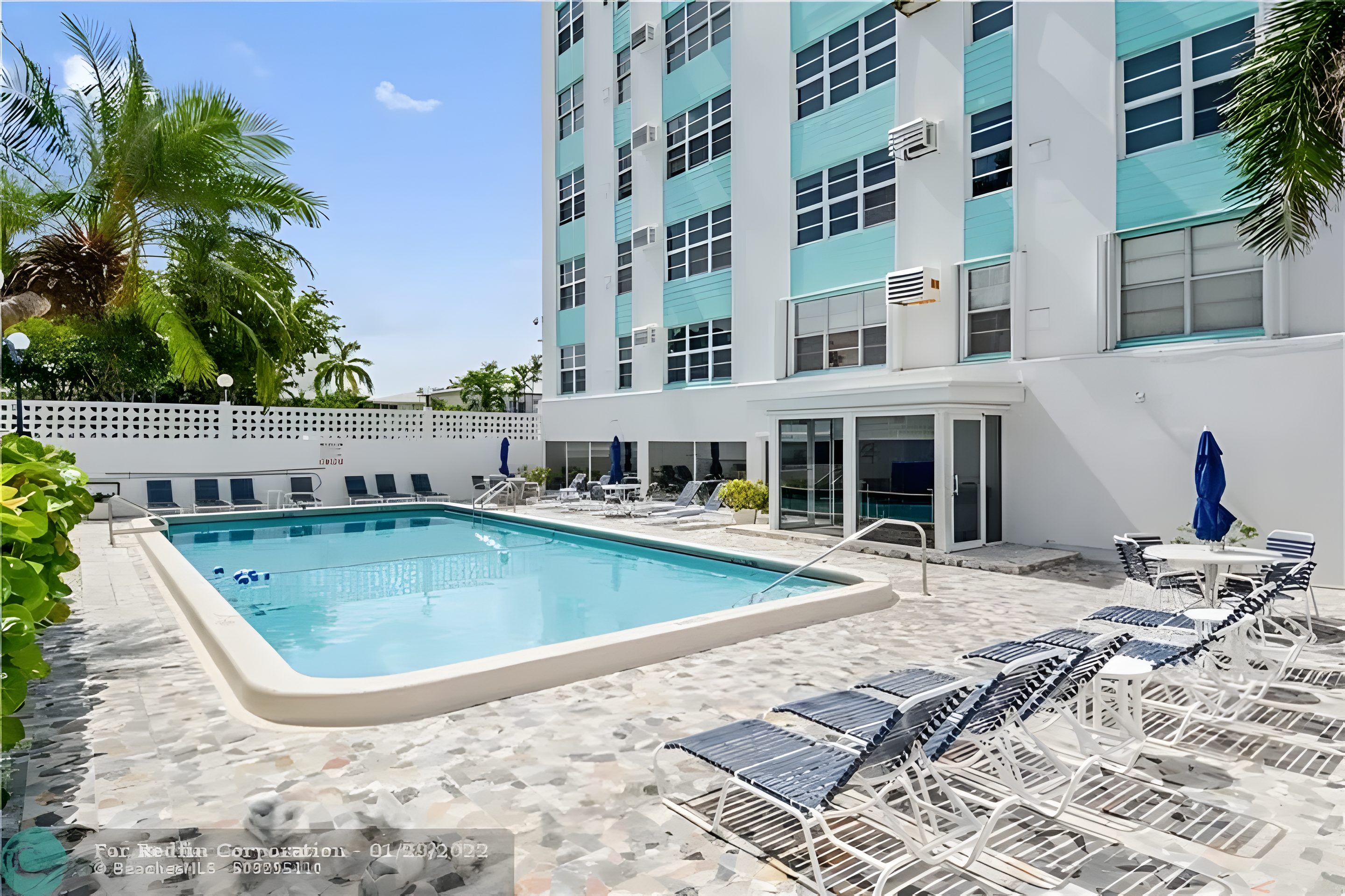 The pool beside the turquoise building, loungers along the deck.
